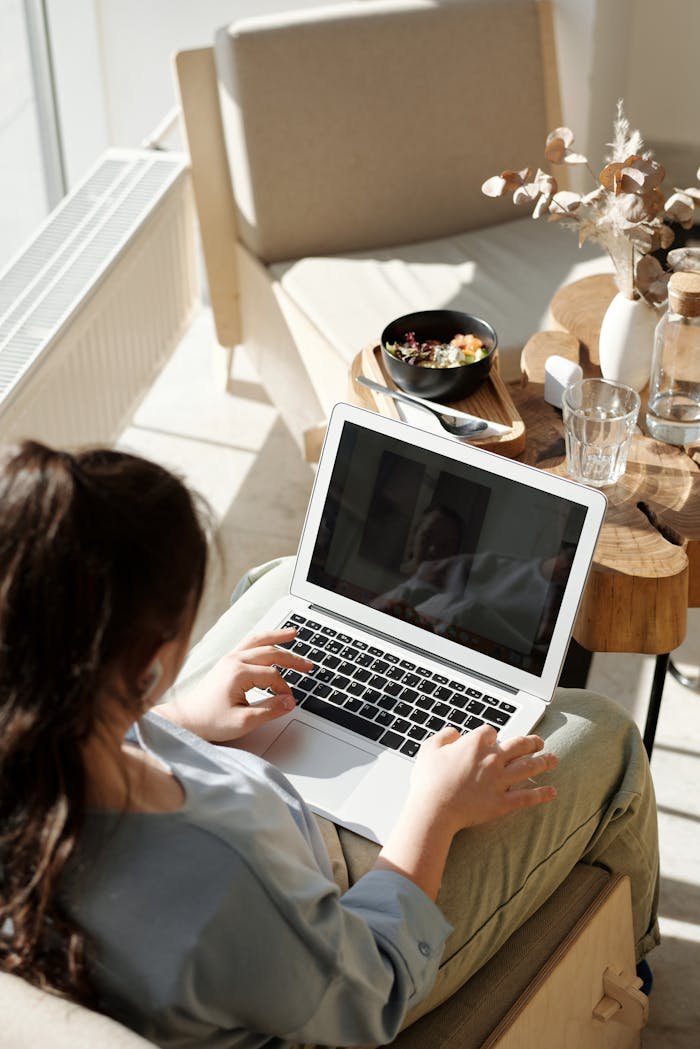 Woman enjoying remote work on a laptop in a cozy home setting with natural light.